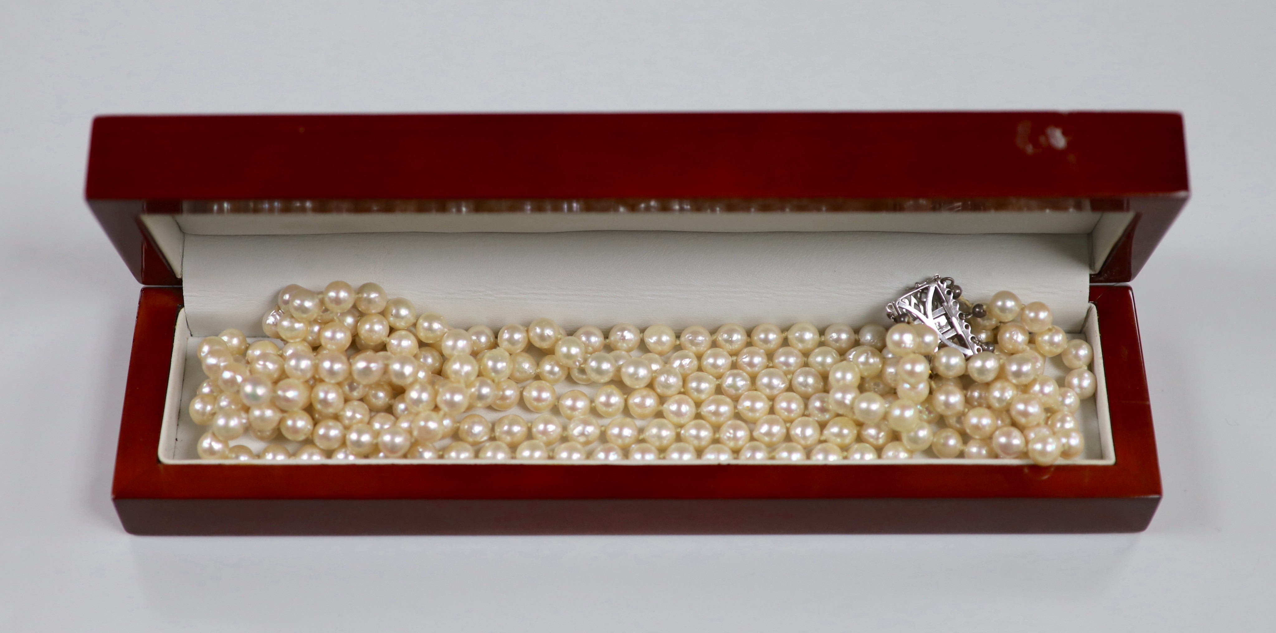A mid to late 20th century triple strand cultured pearl necklace, with pierced 750 white metal and five stone emerald chip set clasp, approximately 56cm.